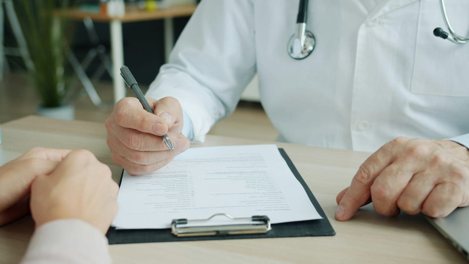 Physician writing on a patient chart during a consultation