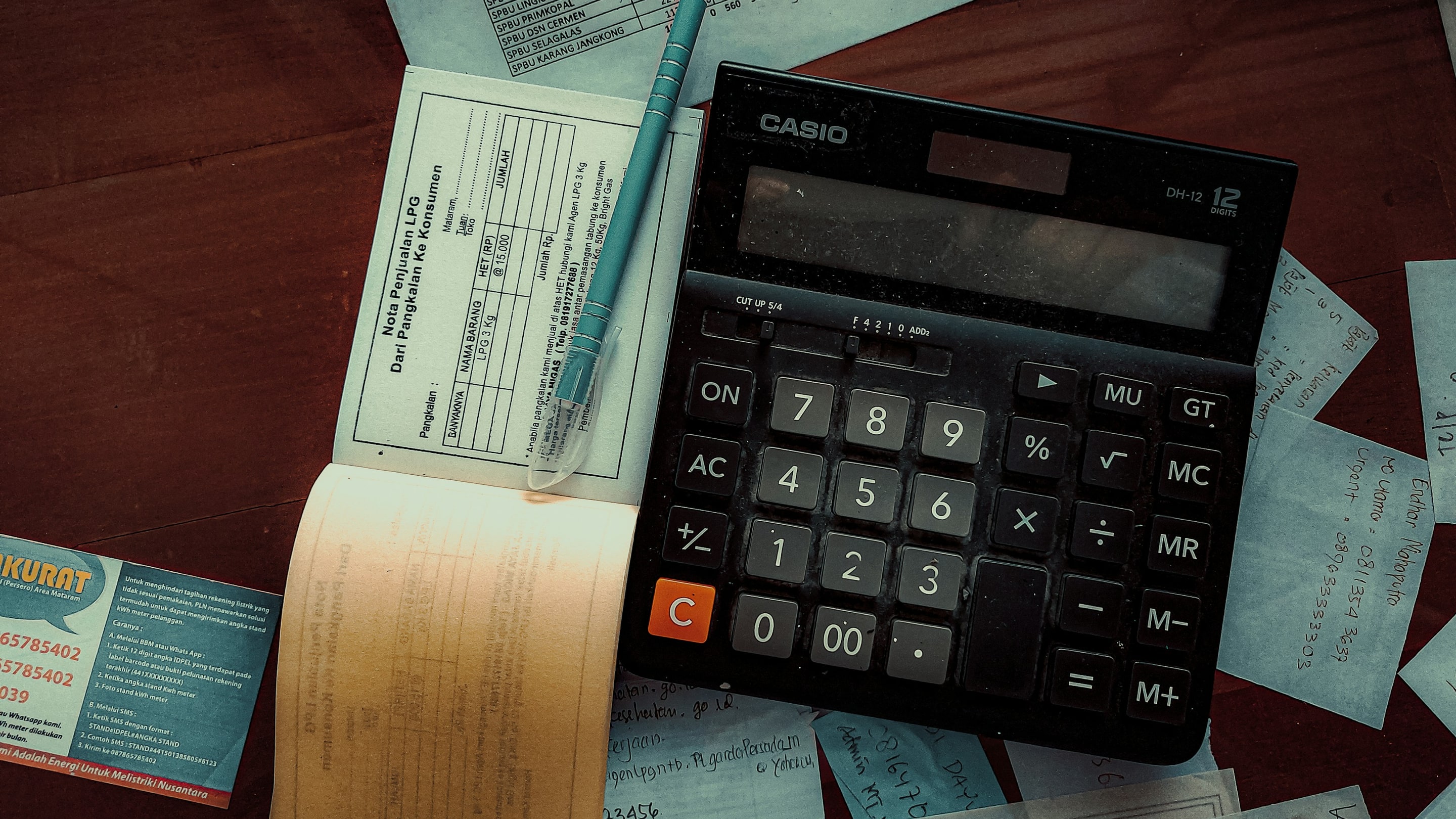 A calculator, a receipt book and a pen on a desk covered with notes