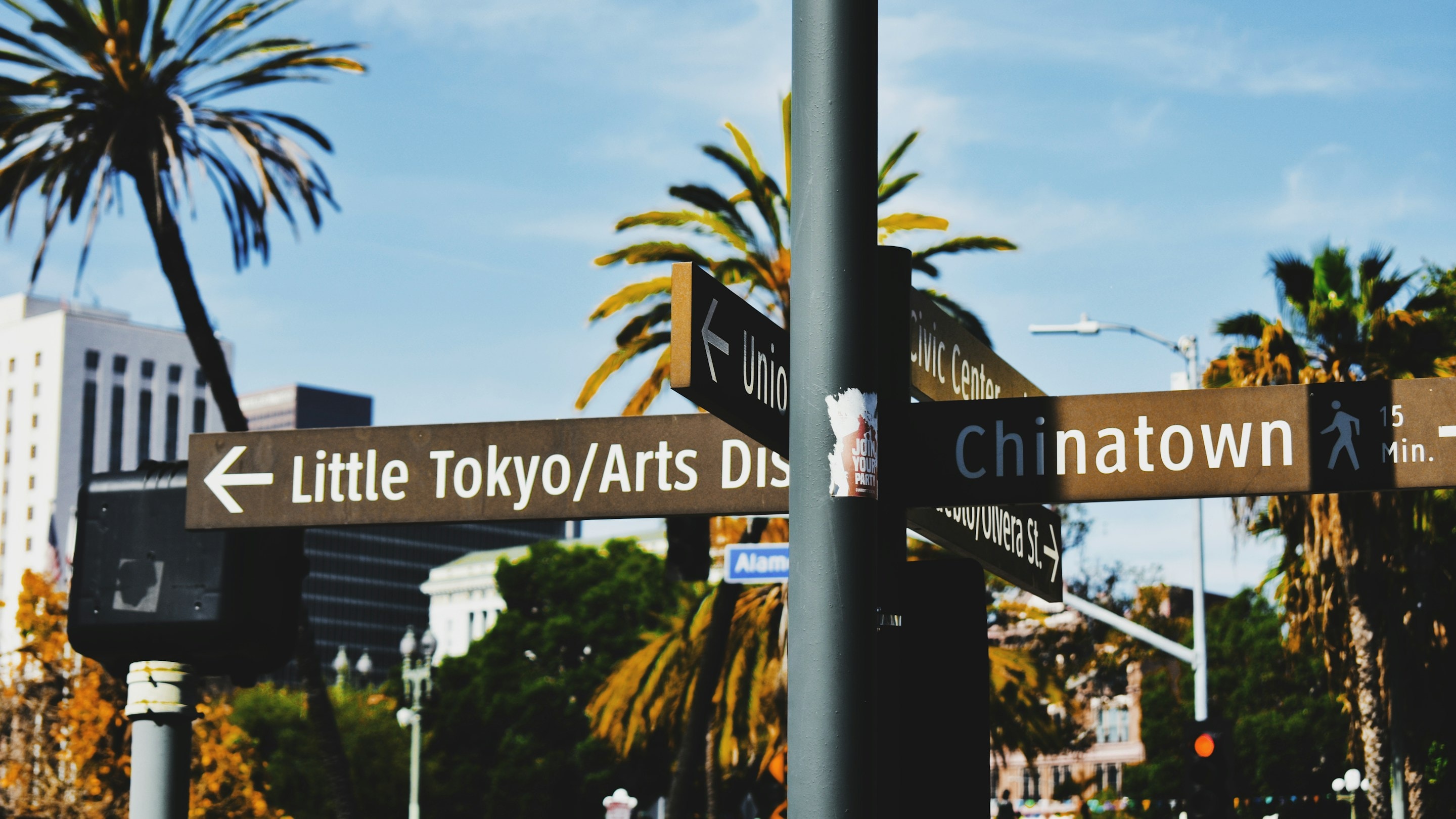 Street signs in downtown Los Angeles pointing to Little Tokyo and Chinatown, with palm trees behind