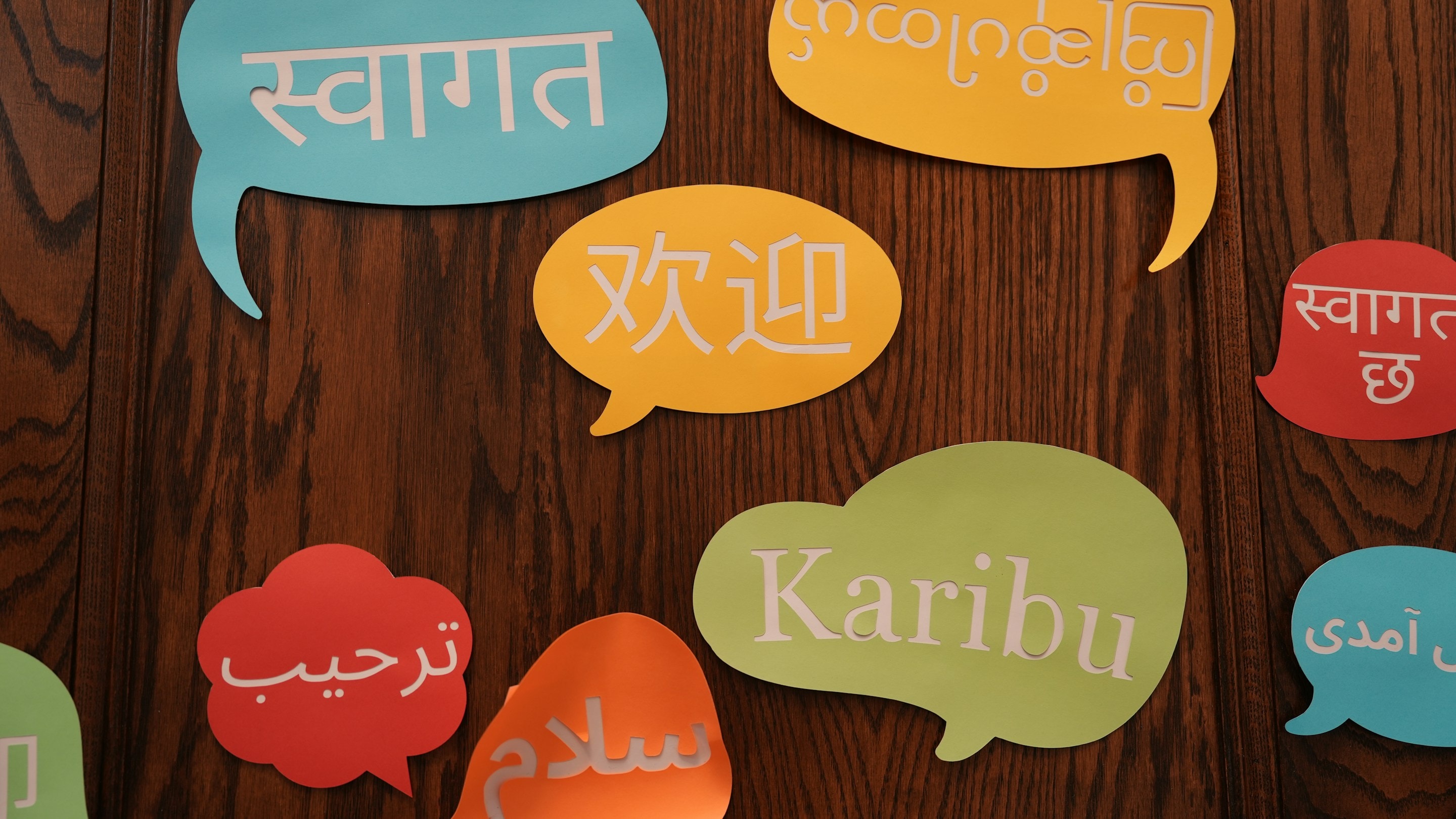 Speech bubbles on a wooden wall saying welcome in Hindi, Chinese, Arabic, Swahili and other languages
