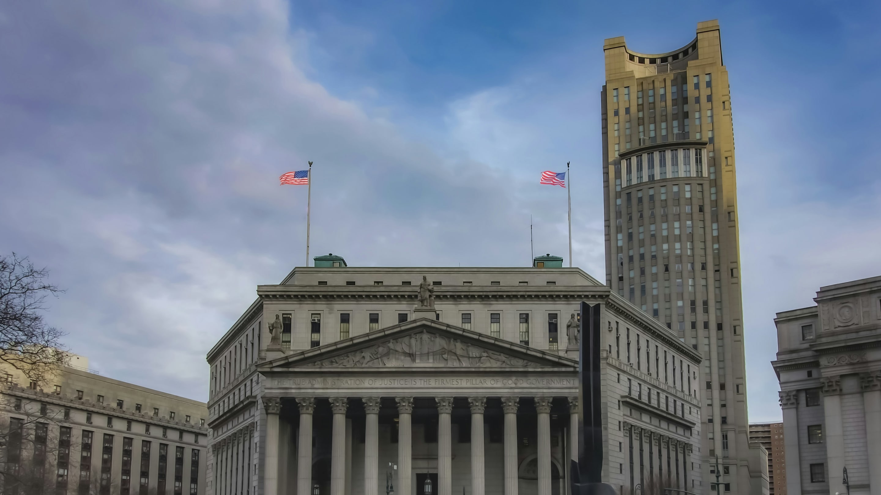 A neoclassical courthouse with American flags on the roof beside a stone office tower